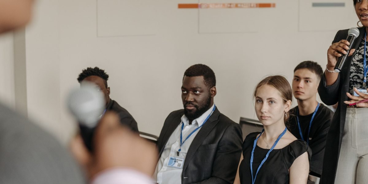 A person in a professional setting engages in a discussion, asking thoughtful and critical questions.
